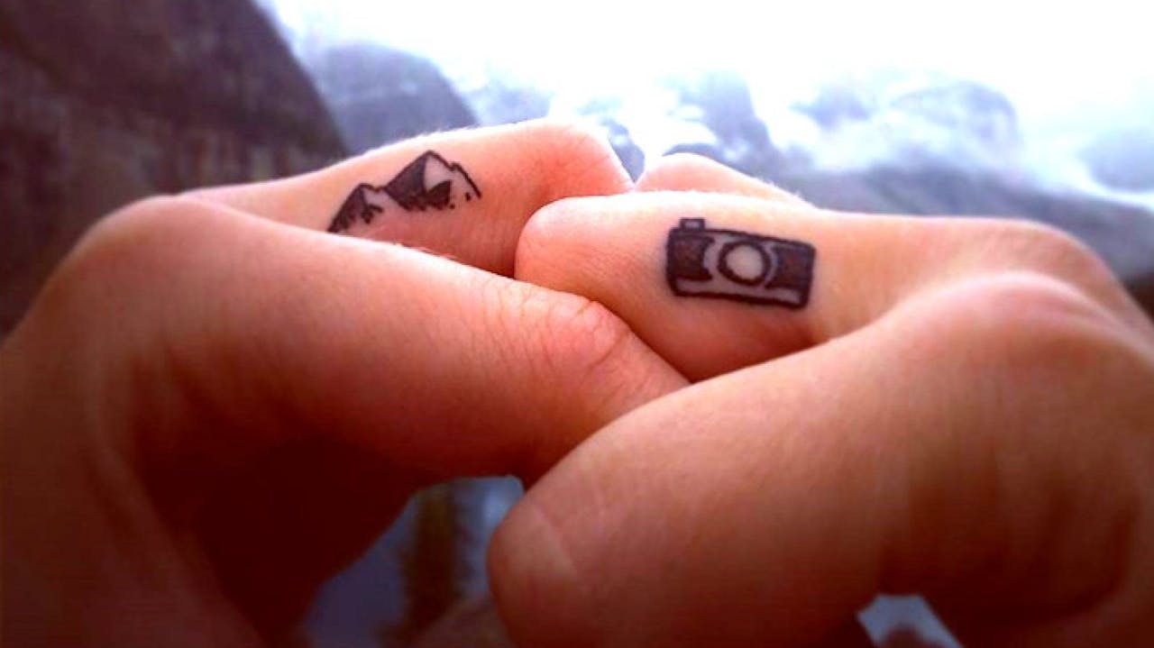 Pequeños tatuajes en el dedo de una montaña y una cámara de fotos.